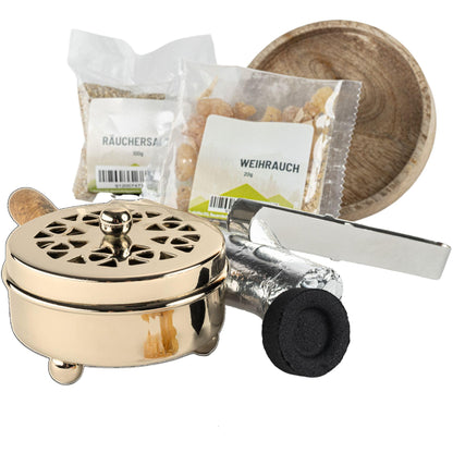 Goldfarbene Räucherpfanne mit Holzgriff neben Räuchersand, Weihrauch, Zange und Kohle