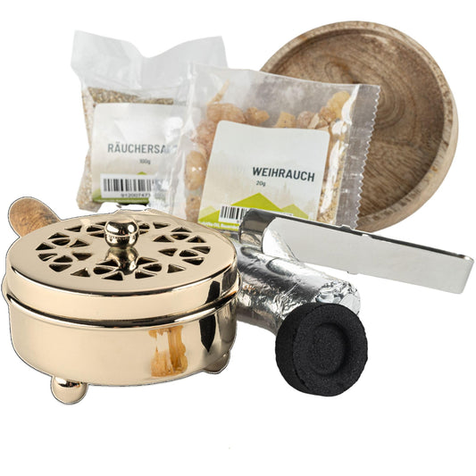 Goldfarbene Räucherpfanne mit Holzgriff neben Räuchersand, Weihrauch, Zange und Kohle