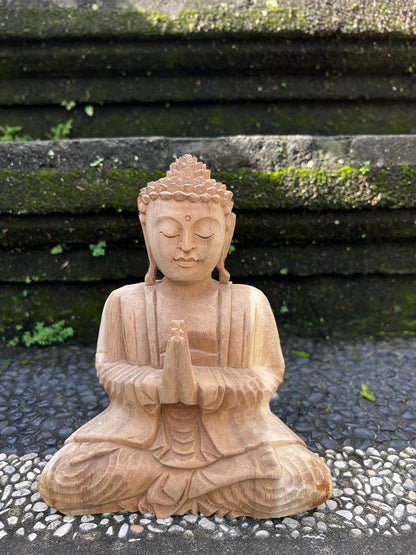 Sitzende Holz-Buddhafigur mit gefalteten Händen vor dunklen Steinstufen