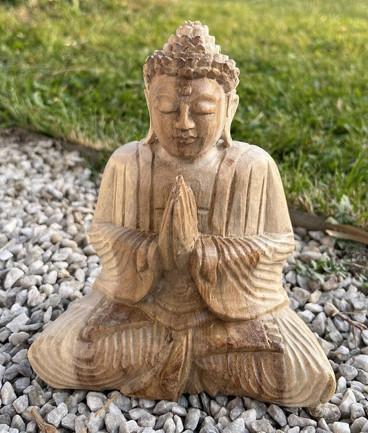 Sitzende Holz-Buddhafigur mit gefalteten Händen auf hellem Kies