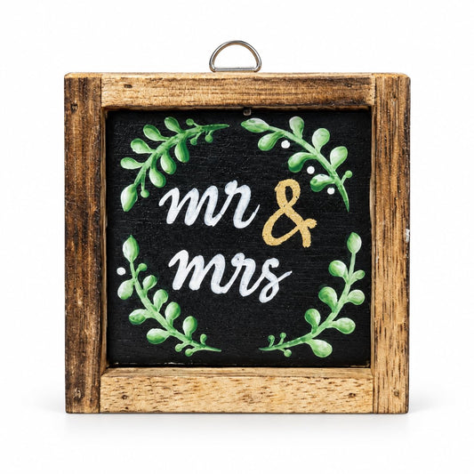 Holzbild mit Mr-&-Mrs-Schriftzug und grünem Blätterkranz auf schwarzem Grund